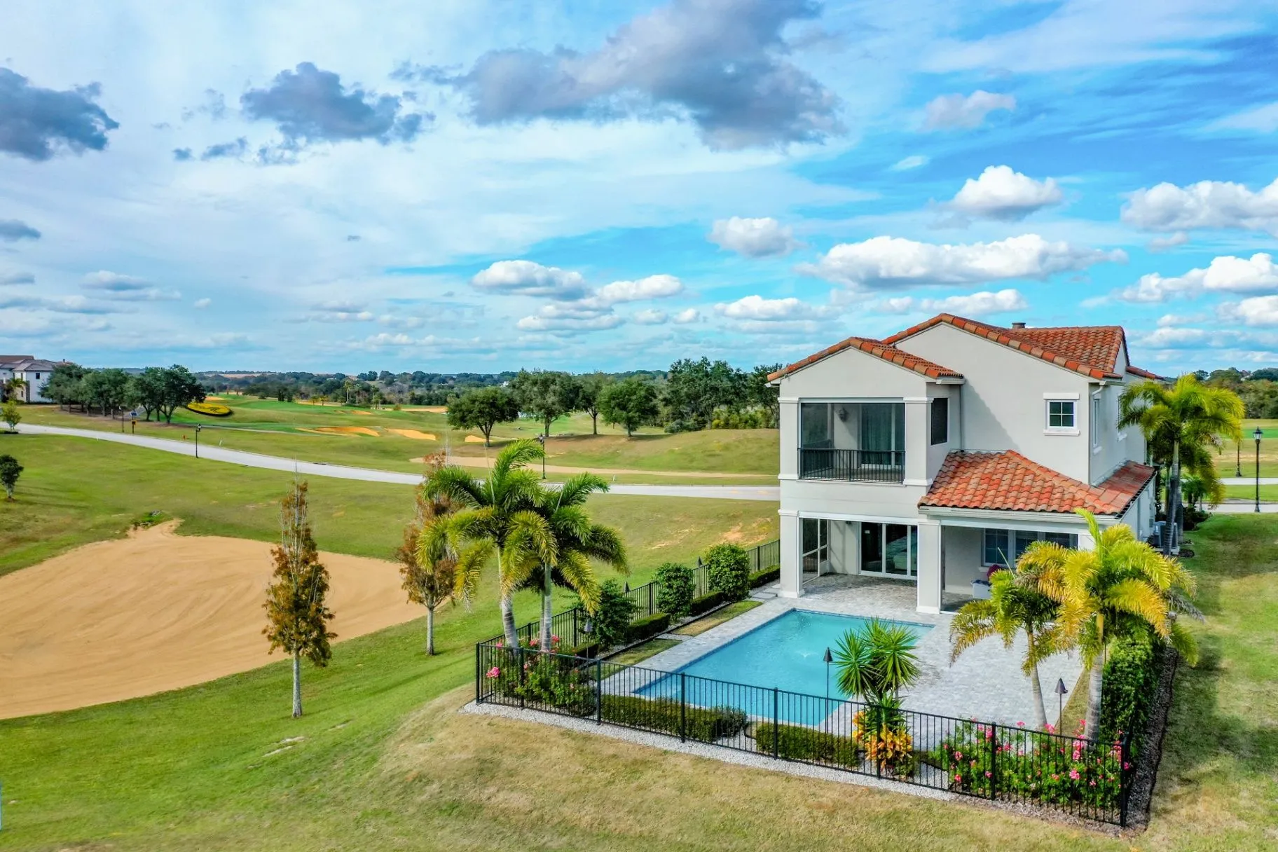 Upscale white home with a terracotta tile roof, swimming pool, palm trees, and landscaped grounds overlooking a golf course